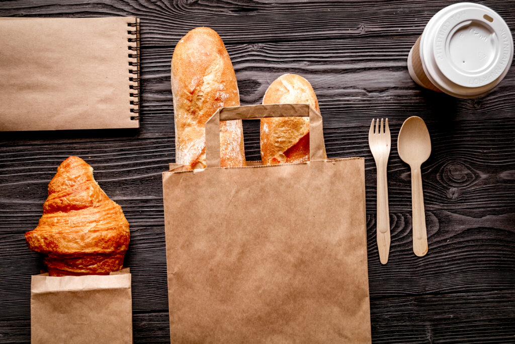 cup coffee and bread in paper bag on wooden background